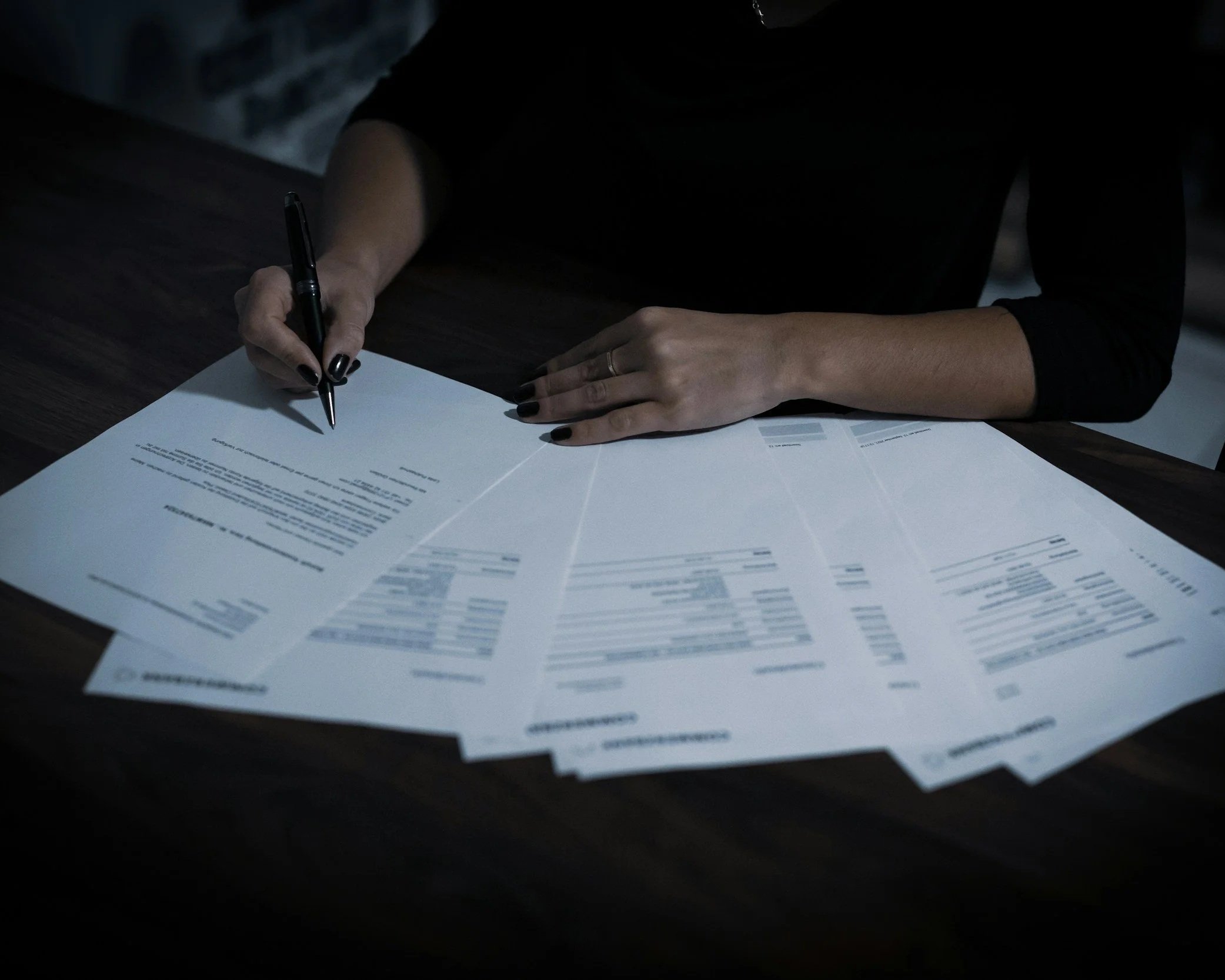 Close-up of hands writing on legal documents on a dark wooden table.