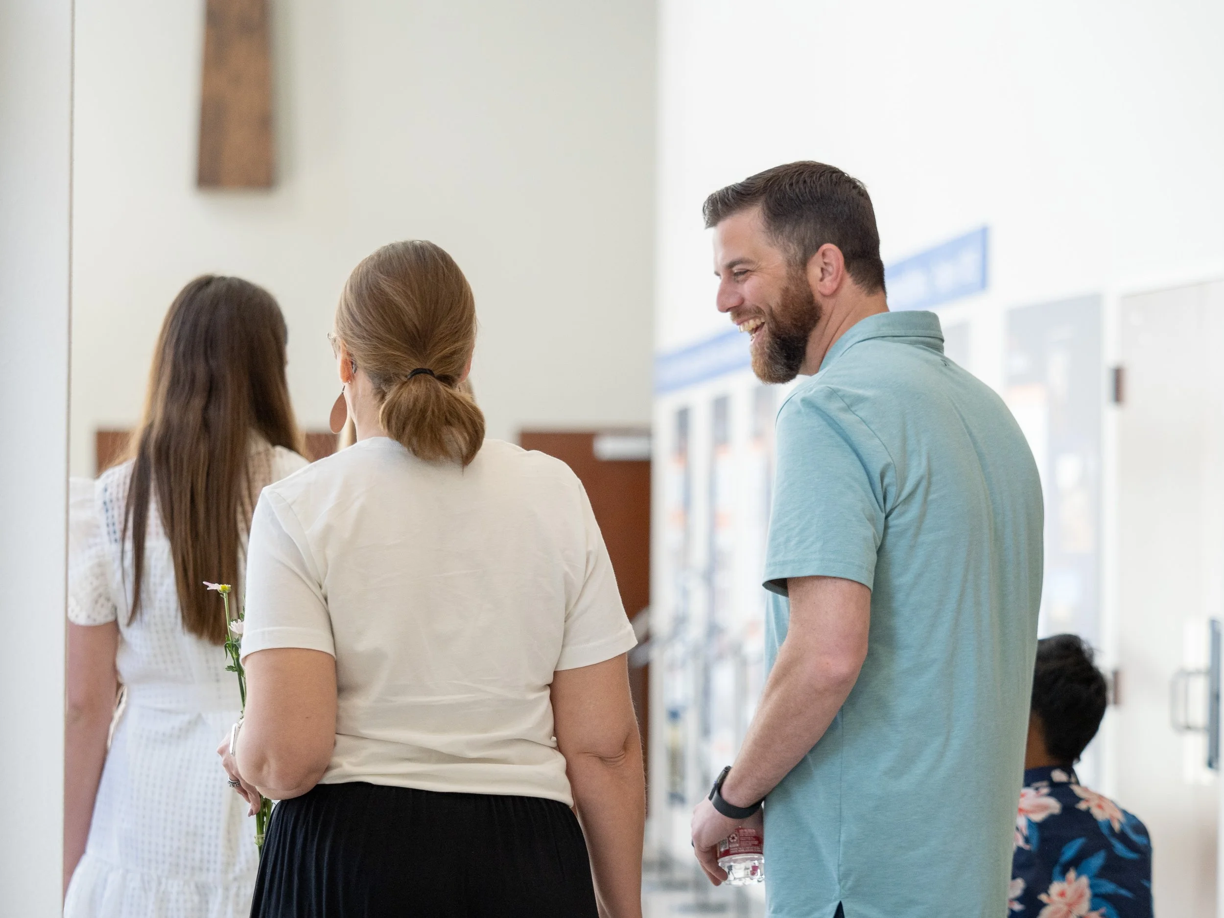 Three people talking and smiling in a public indoor space, with vending machines in the background.