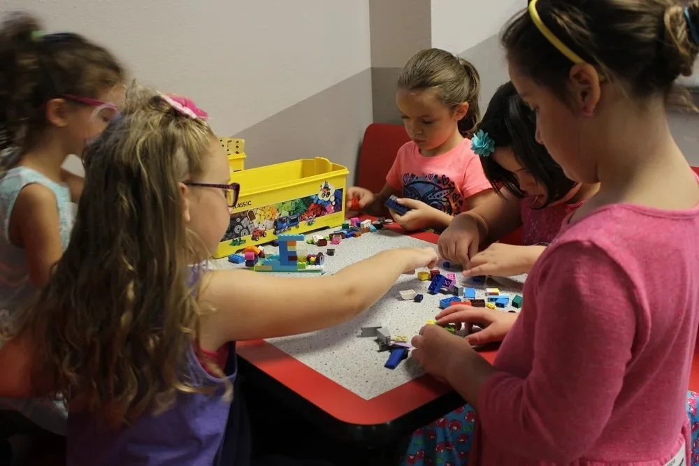Group of young girls playing with building blocks at a table in an indoor setting.