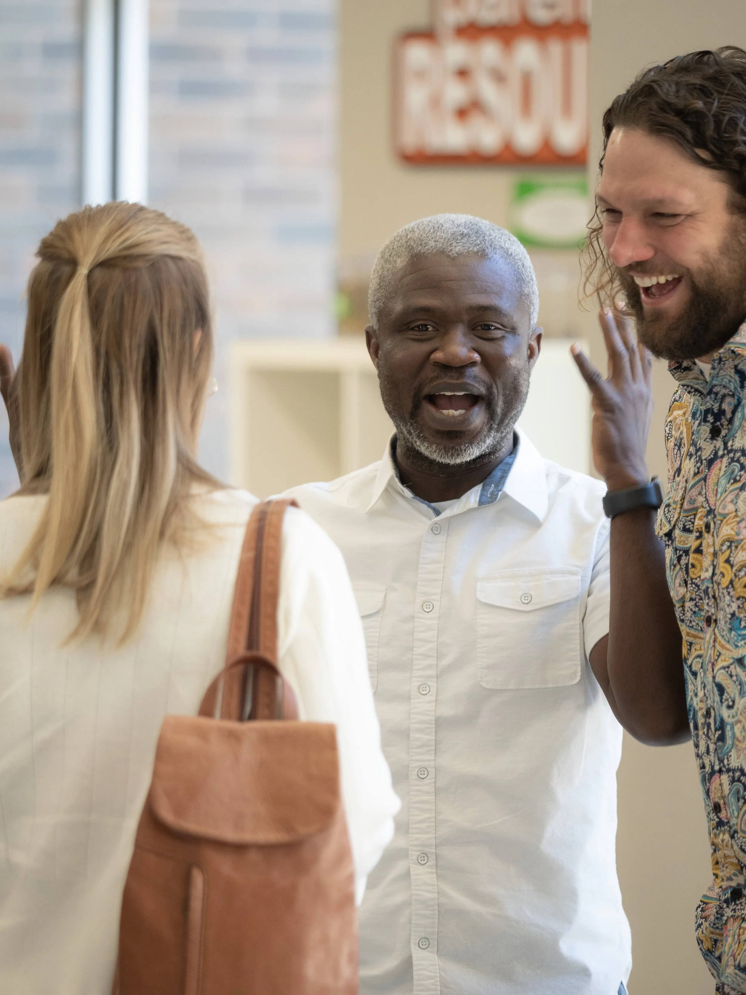 Three people engaged in a lively conversation indoors, smiling and gesturing animatedly.