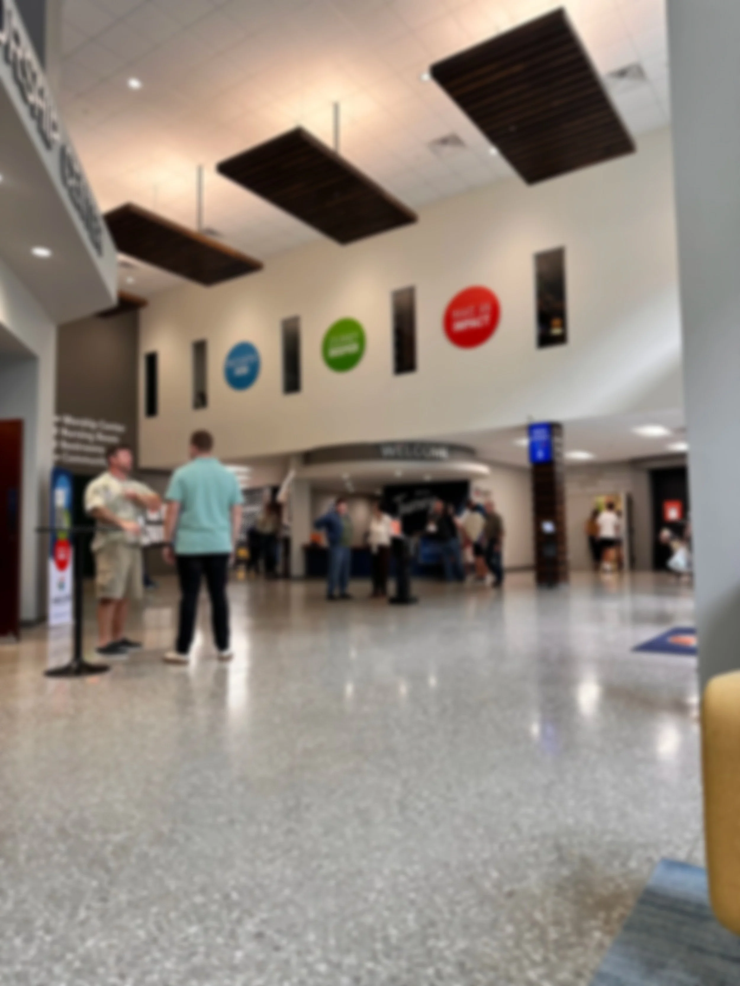 People standing in line and talking inside a modern airport with signs and a check-in area in the background.
