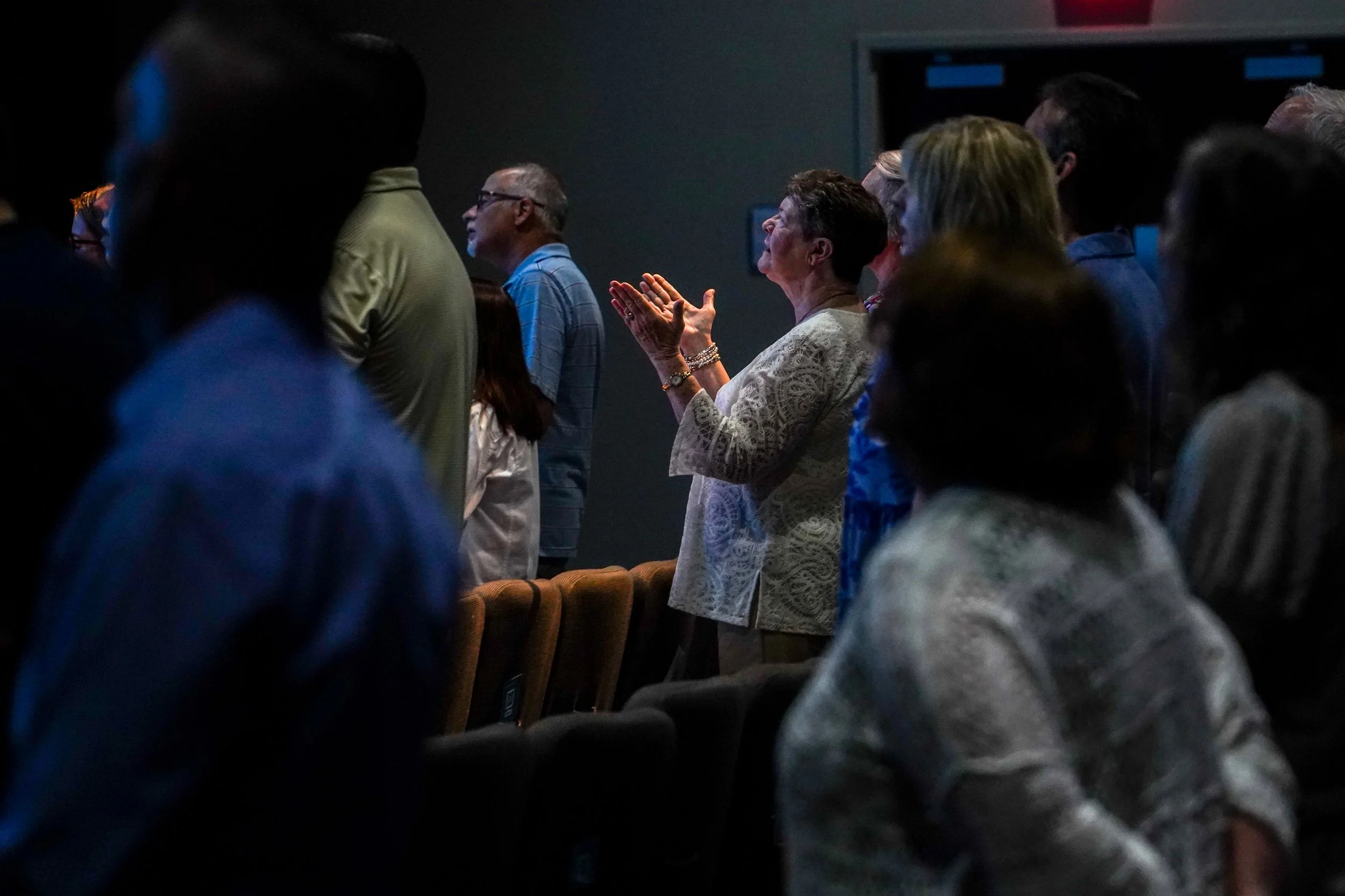 People standing and clapping in a darkened room, likely at an event or gathering.