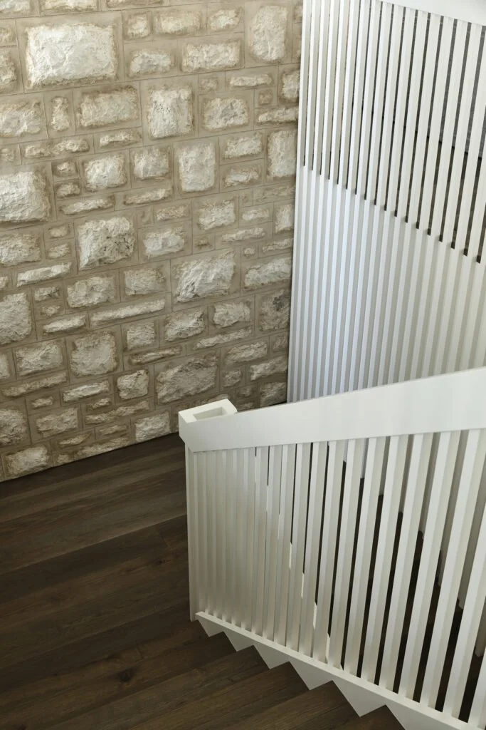 View of a staircase with a white railing, next to a brick wall with beige and white stones, and wooden flooring.