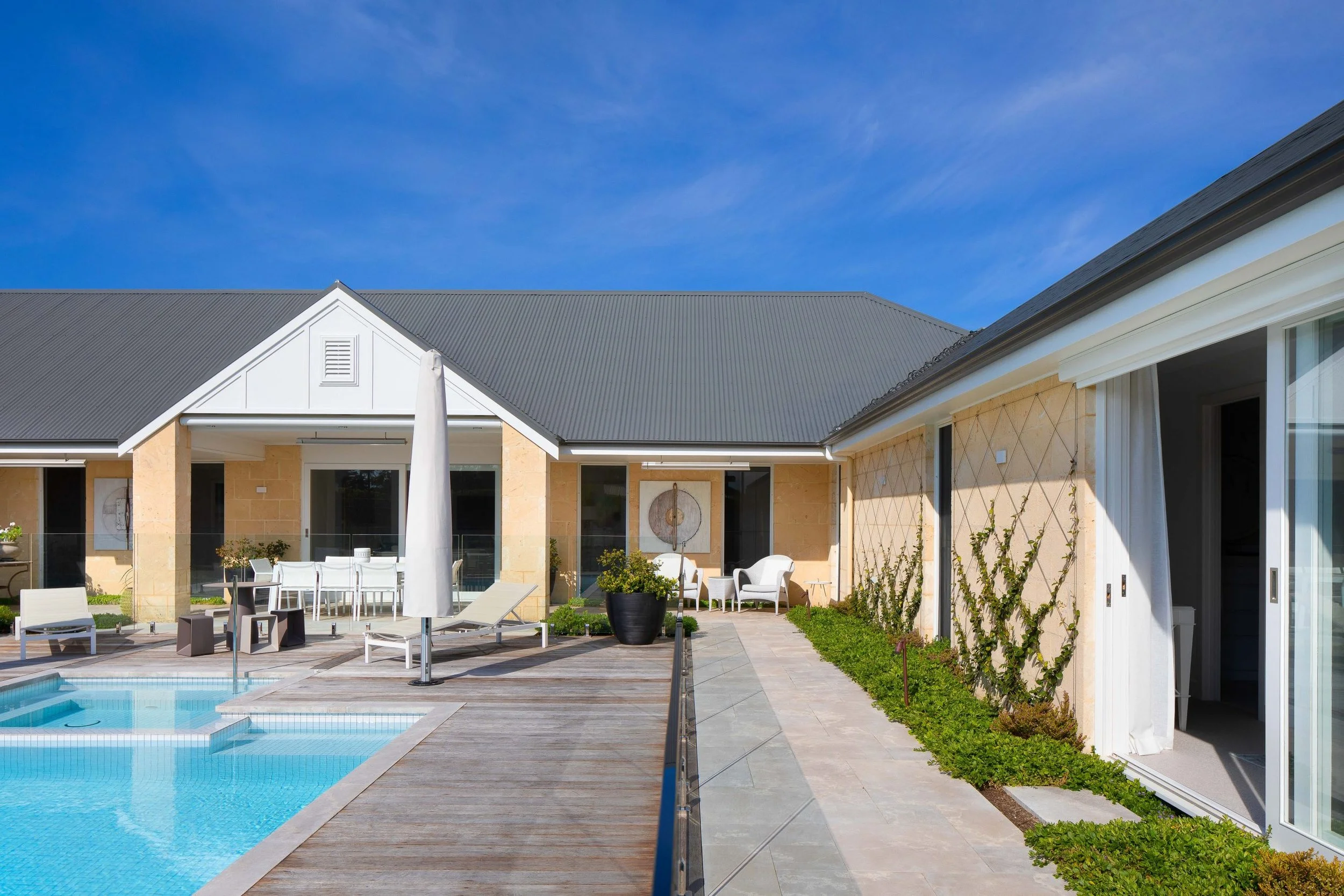 A modern house with a backyard pool, outdoor furniture, potted plants, and a bright blue sky