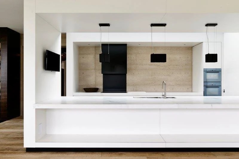 Modern kitchen with white counter, black pendant lights, beige textured wall, and built-in appliances.