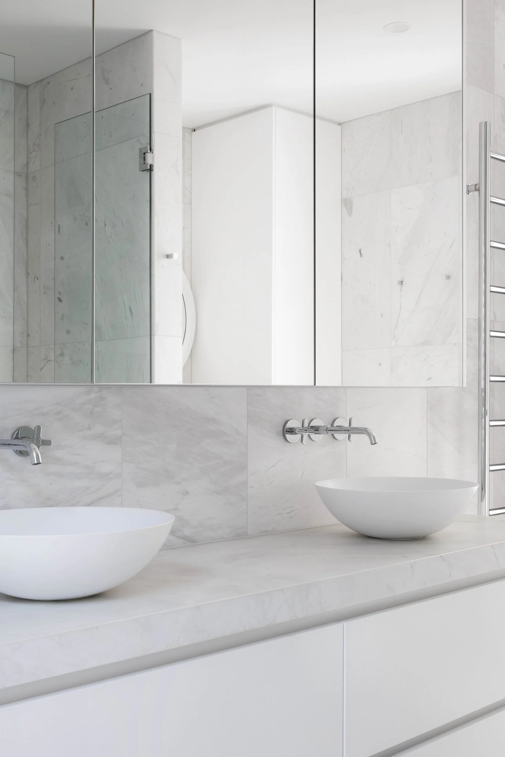 Modern bathroom with a large mirror, two white basin sinks, a marble countertop, and a heated towel rail on the wall.