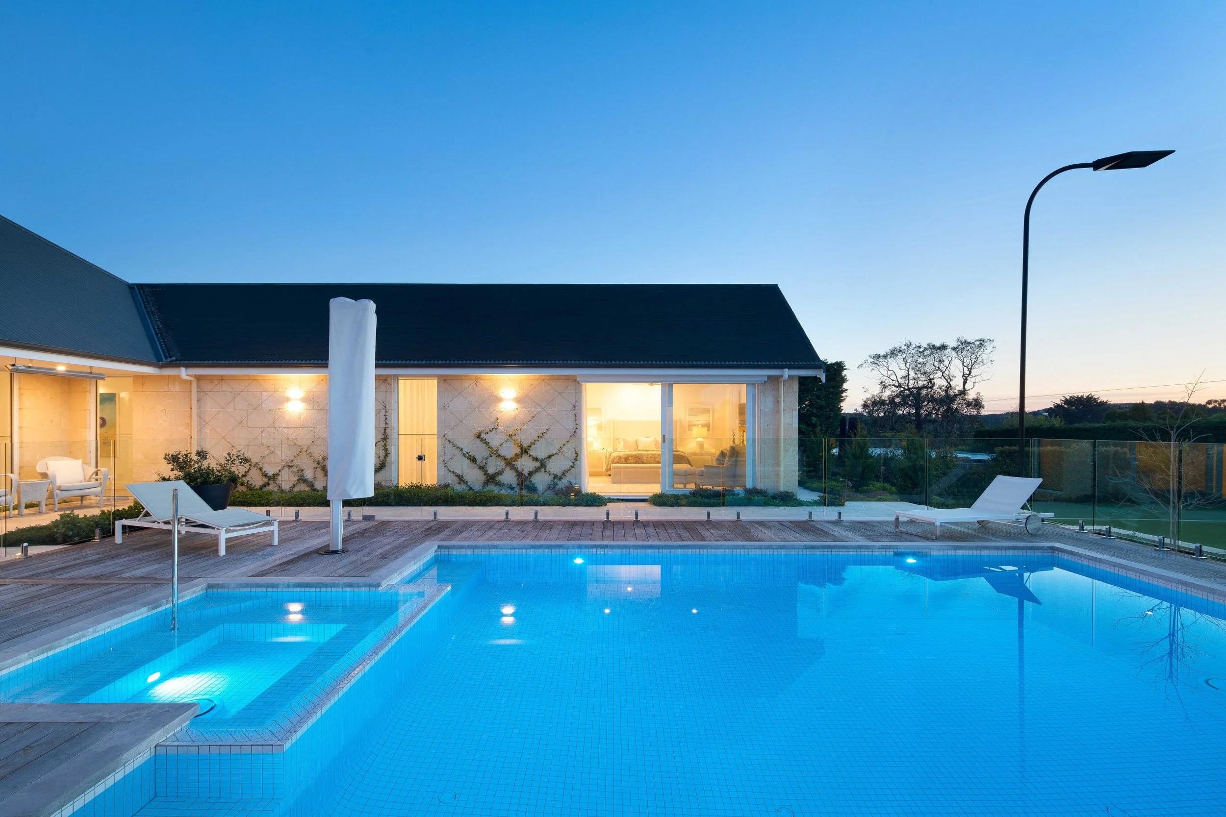 Luxury house with a swimming pool and outdoor lounge area during dusk, illuminated by exterior lights.