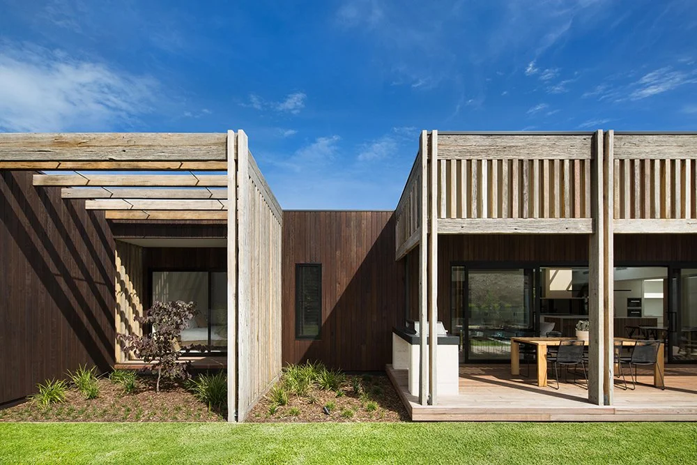 Modern house with a wooden patio and garden area under a blue sky.