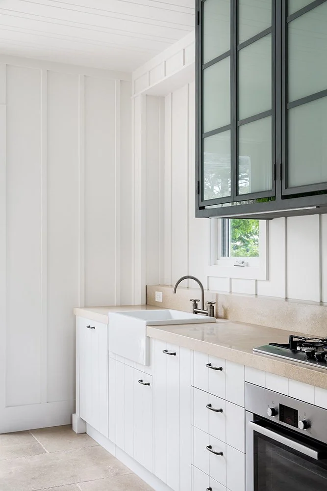 Modern kitchen with white cabinets, beige countertops, a farmhouse sink, and dark green upper cabinets over a small window.