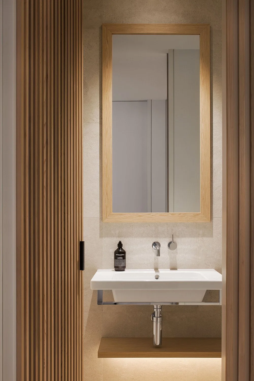 Modern bathroom with a white rectangular sink, a large wooden framed mirror, and wooden slat accents on the left wall.