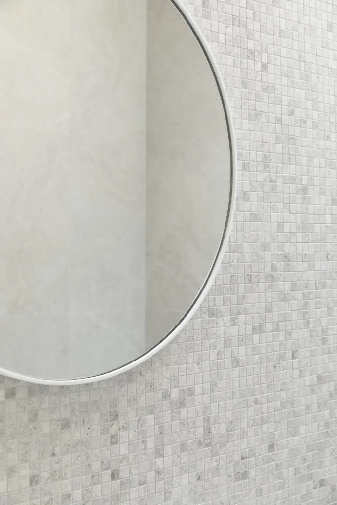 Close-up of a bathroom mirror mounted on a tiled wall in a bathroom.