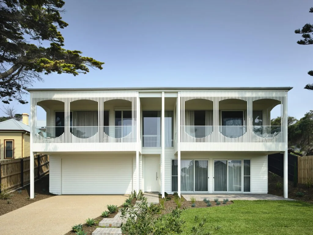 Modern two-story house with rounded balconies, white exterior, small front yard, and a gravel driveway.