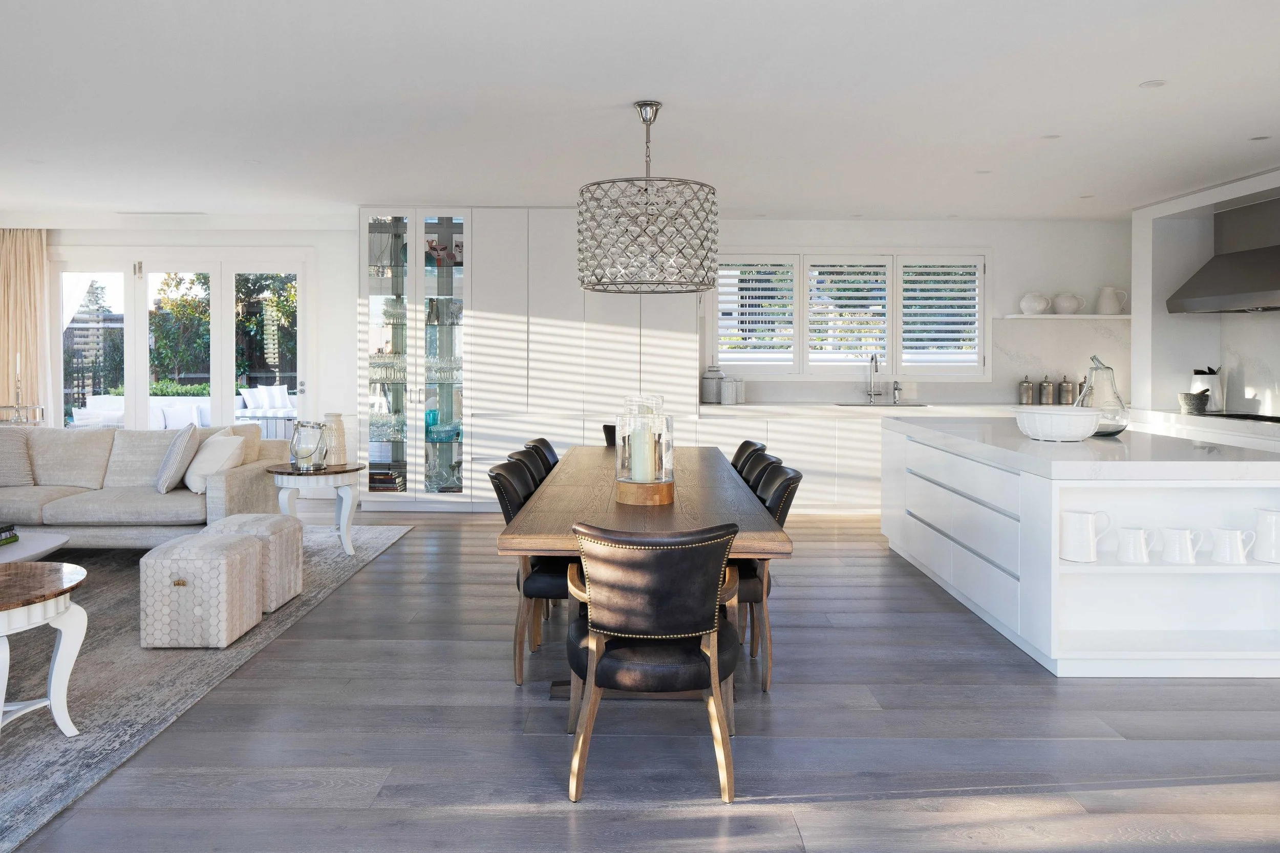 Modern open-concept living room and kitchen with white walls, hardwood floors, a dining table with six black chairs, and a beige sofa.
