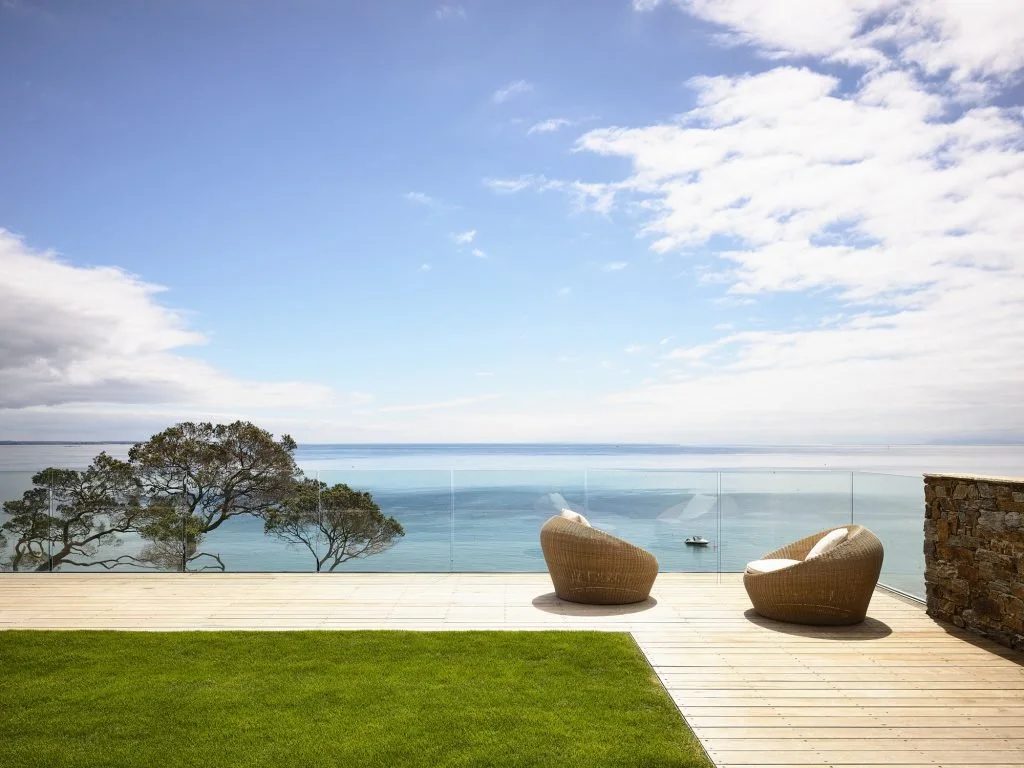 Outdoor patio with two wicker chairs overlooking a body of water and a partly cloudy sky.