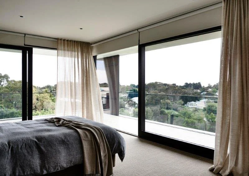 A bedroom with large sliding glass doors overlooking a green landscape and neighborhood.