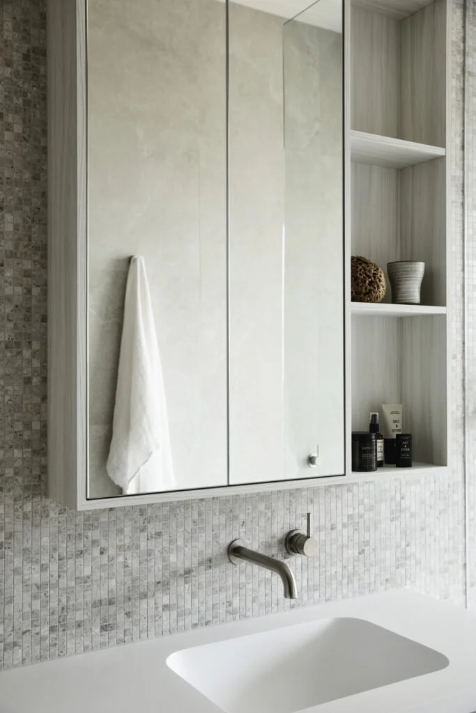 Bathroom with a white sink, a mirrored cabinet with a white towel hanging on the side, and open shelves with decorative items and toiletries.