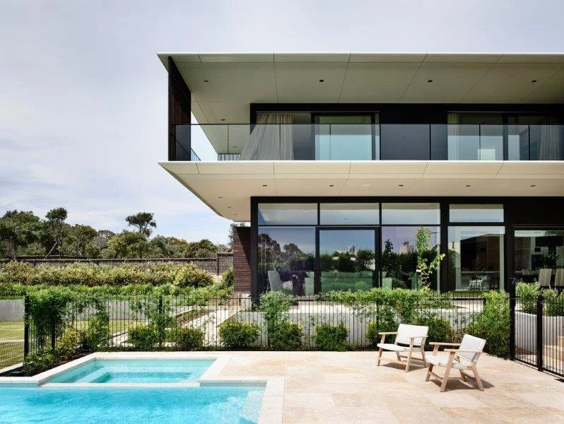 Modern house with a balcony, glass windows, and a backyard featuring a swimming pool and outdoor seating area.