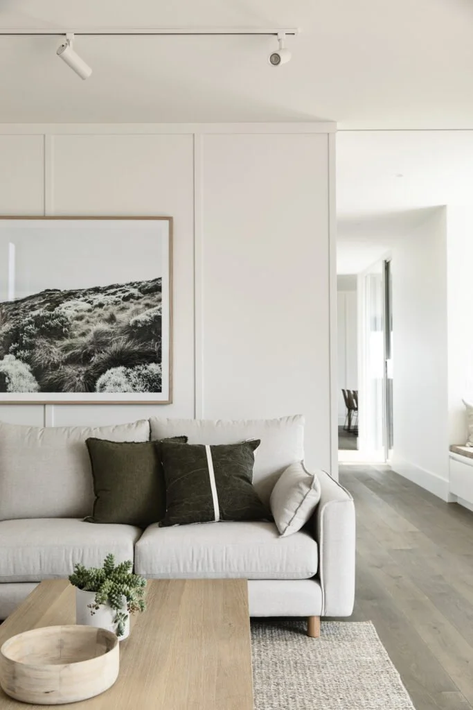 Living room with a white sofa, black and white landscape artwork, wooden coffee table with a plant, and a side table with a chair by a window.