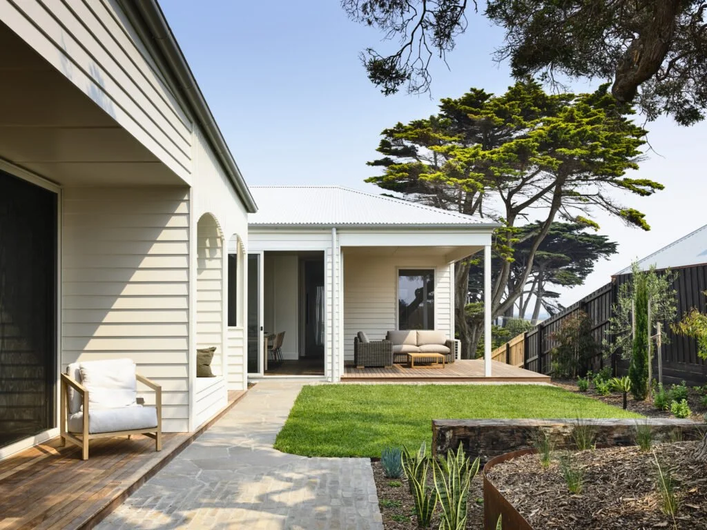 Modern house with a backyard patio, outdoor seating area, green grass, trees, and a blue sky.