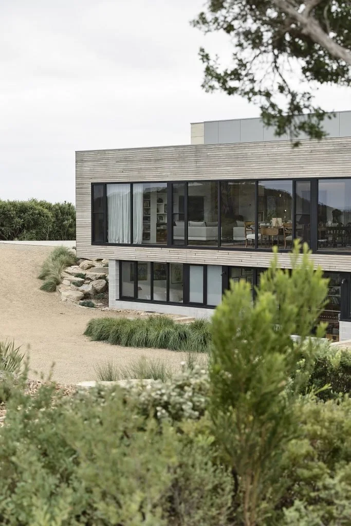 Modern house with large windows, situated on a gentle slope with minimal landscaping and surrounding greenery.