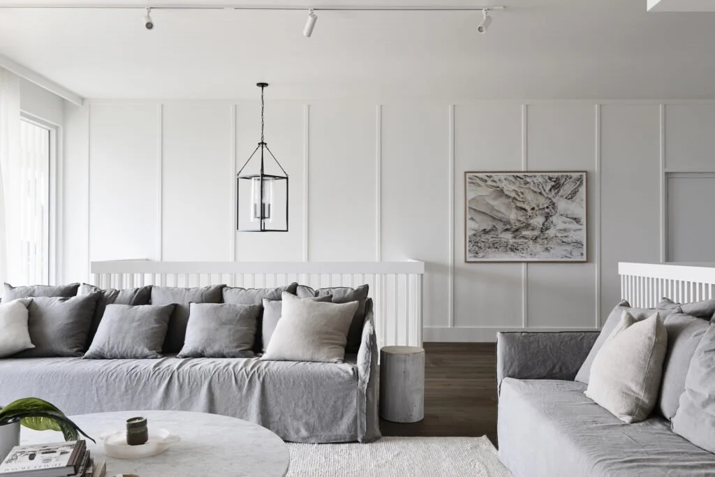 Living room with white walls, gray sofas with cushions, a round coffee table, abstract wall art, and minimalist lighting.