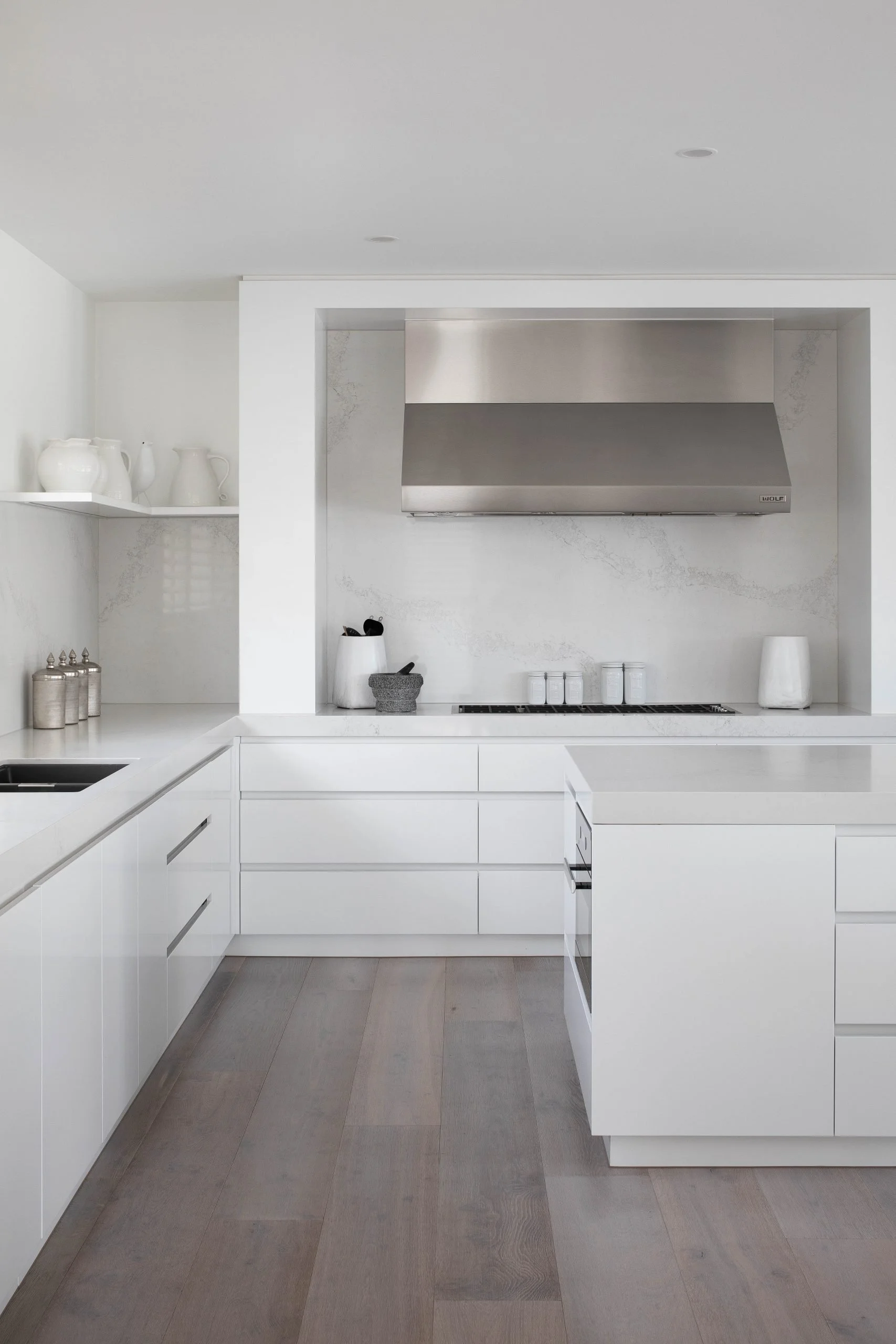 Modern white kitchen with built-in cabinetry, stainless steel range hood, and minimalist decor.