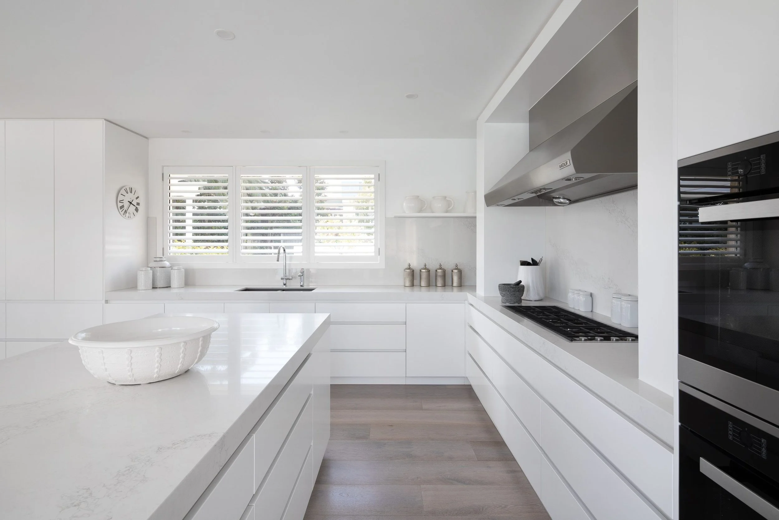 Bright modern white kitchen with large window, stainless steel appliances, and minimalist decor