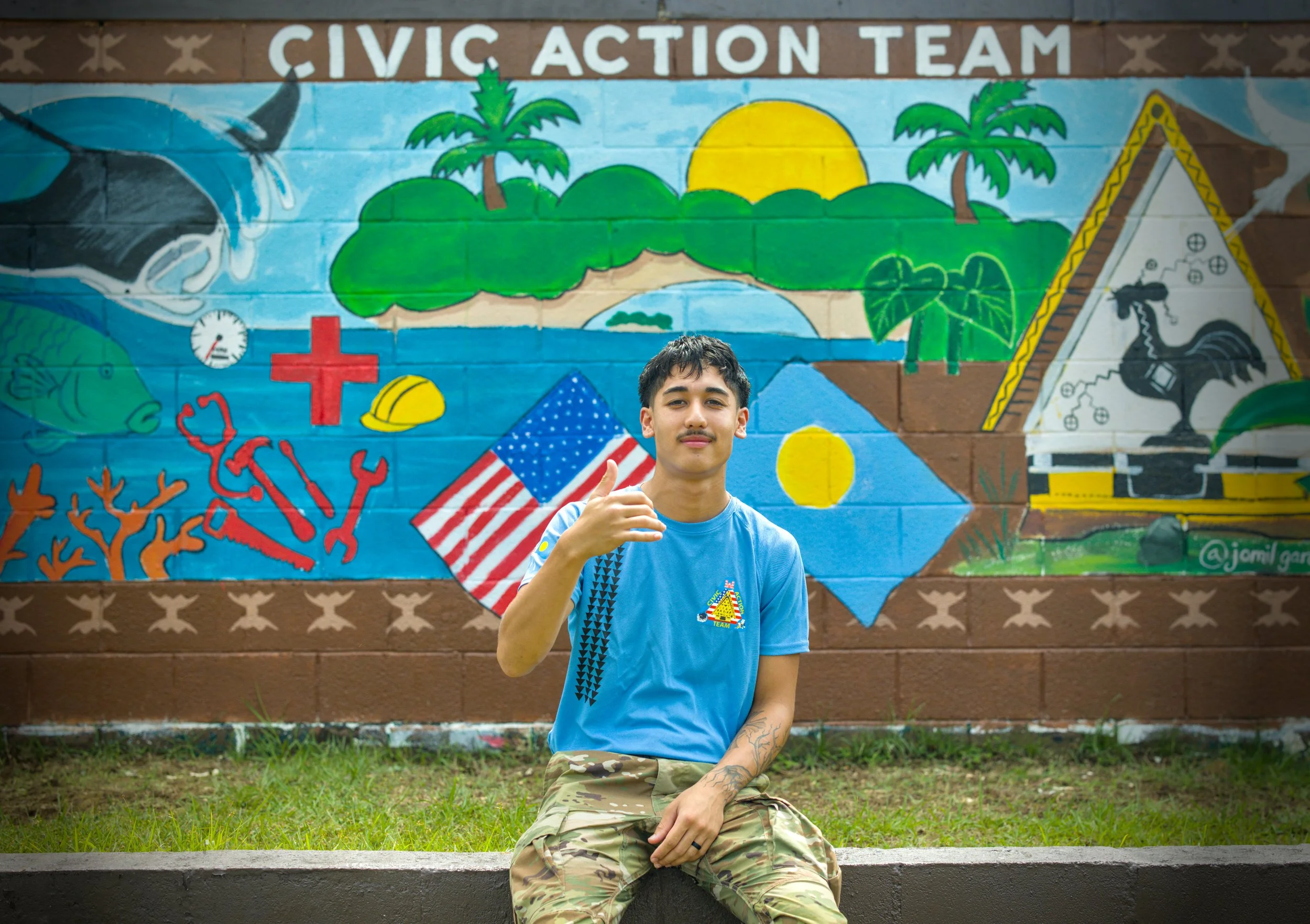 A U.S. Army soldier in camouflage uniform standing against a plain beige wall.
