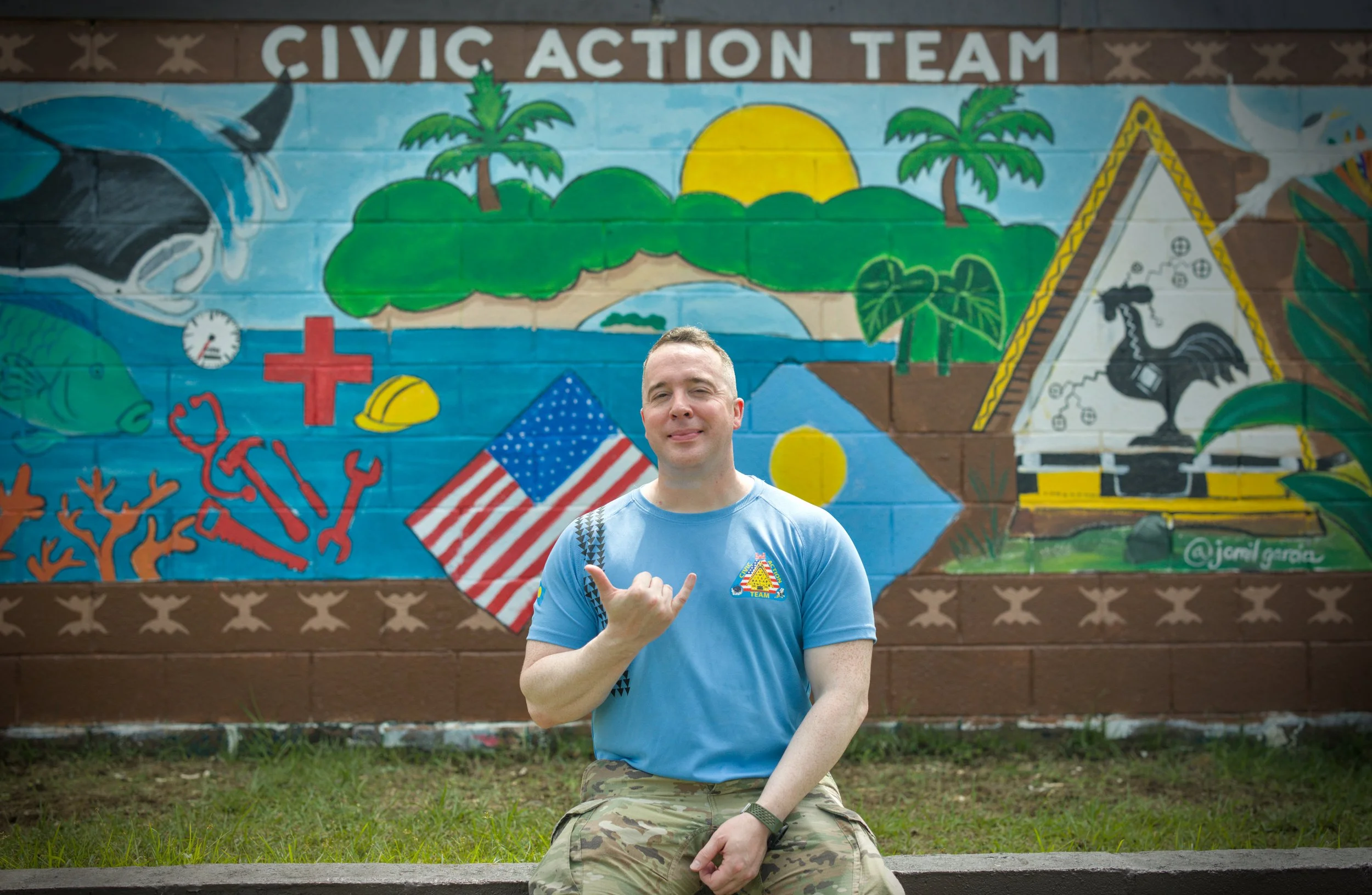 A young male U.S. Army soldier in camouflage uniform standing against a beige wall, facing forward with a serious expression.