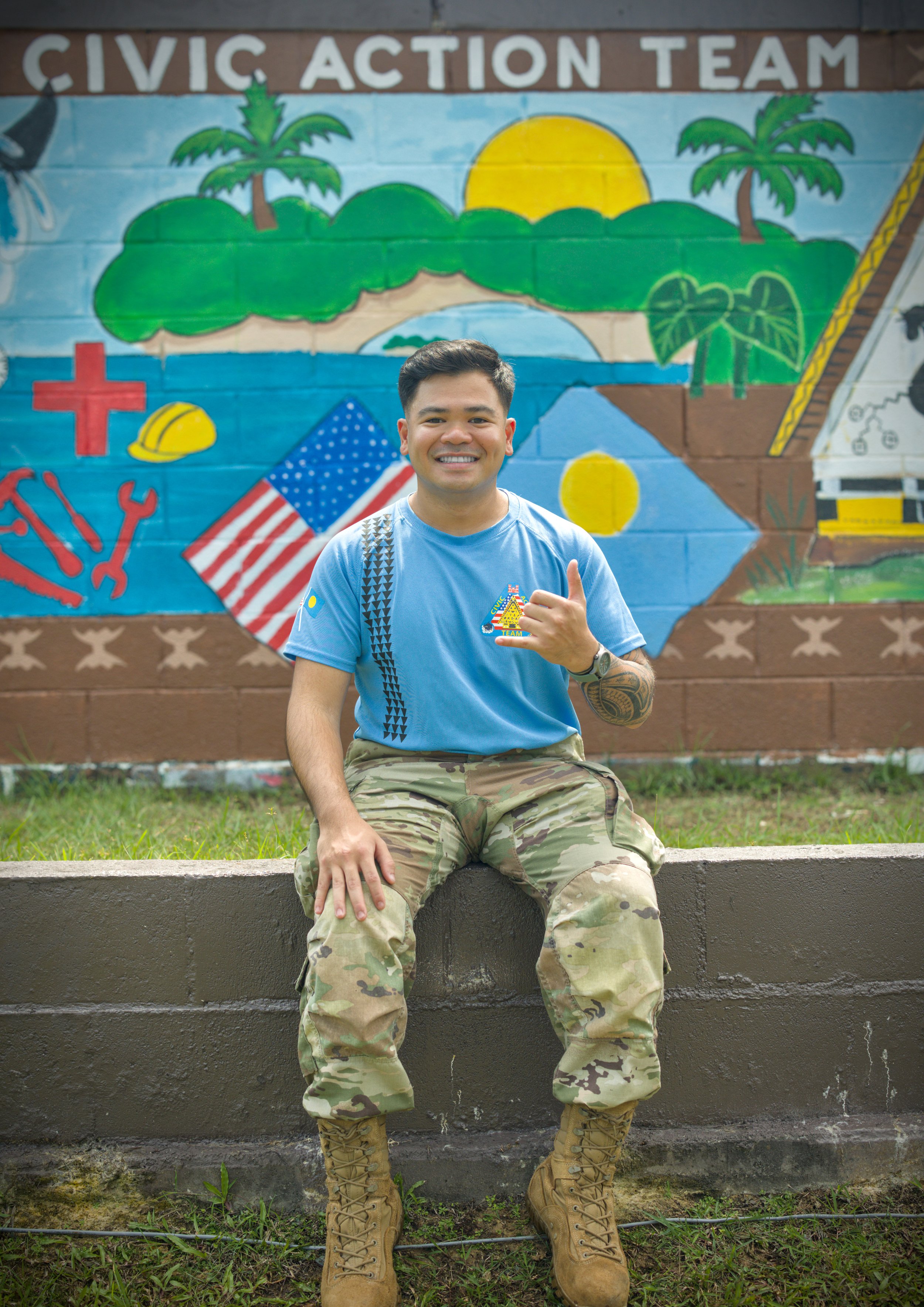 A male U.S. Army soldier in camouflage uniform standing against a beige wall.