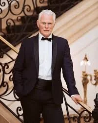 Man in tuxedo standing on staircase with ornate railing