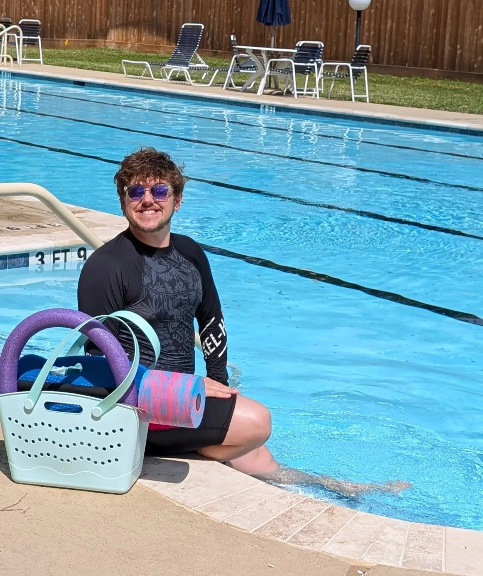 Coach David smiling poolside with swim gear and toys.