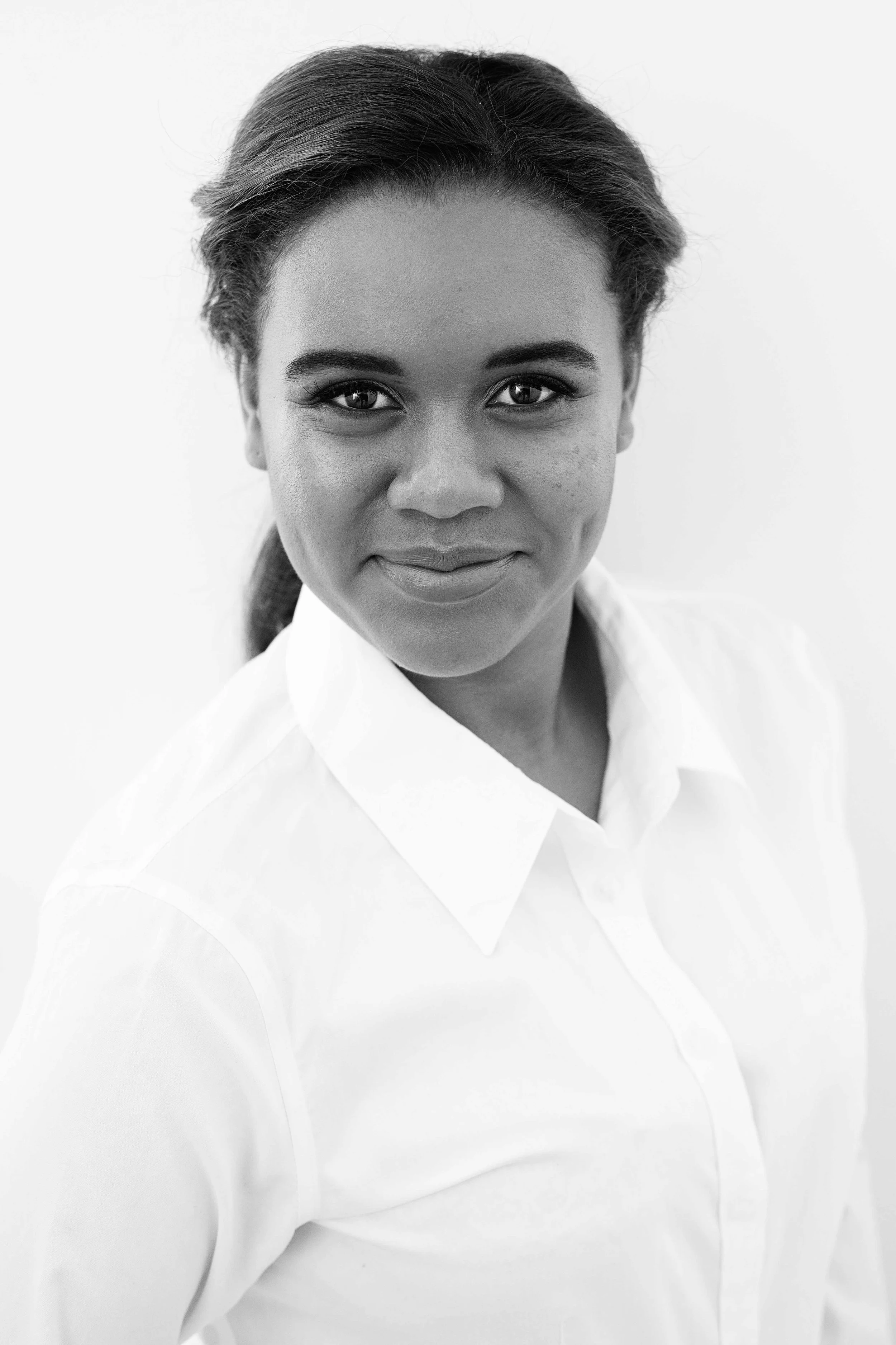 Black and white portrait of a woman with a confident smile, wearing a white collared shirt, with her hair tied back.