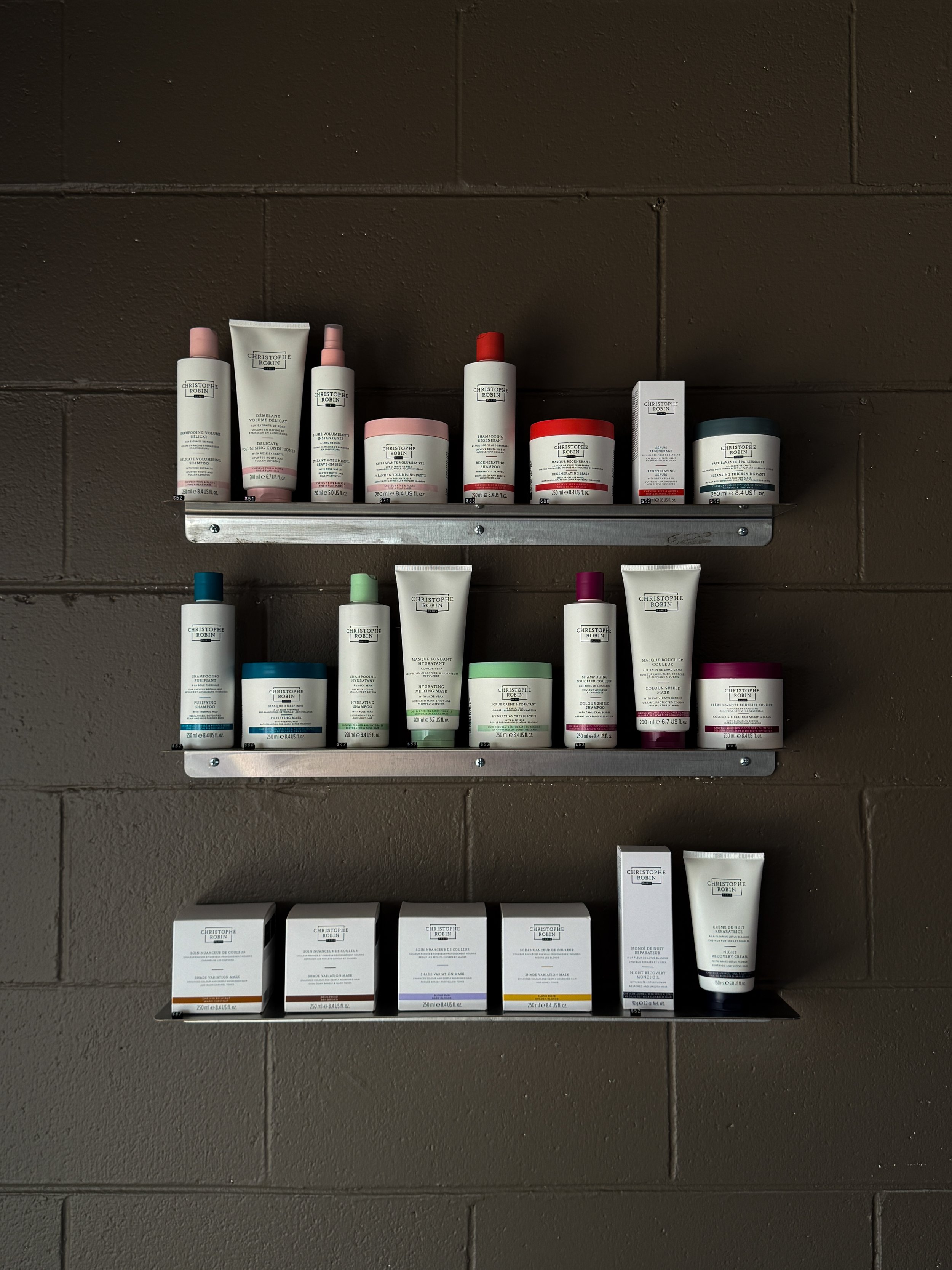 Display of Christophe Robin hair care products on metal shelves against a brown wall.
