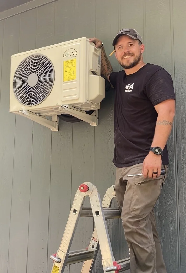 A man standing on a ladder installing or repairing an outside air conditioning unit attached to a wall.