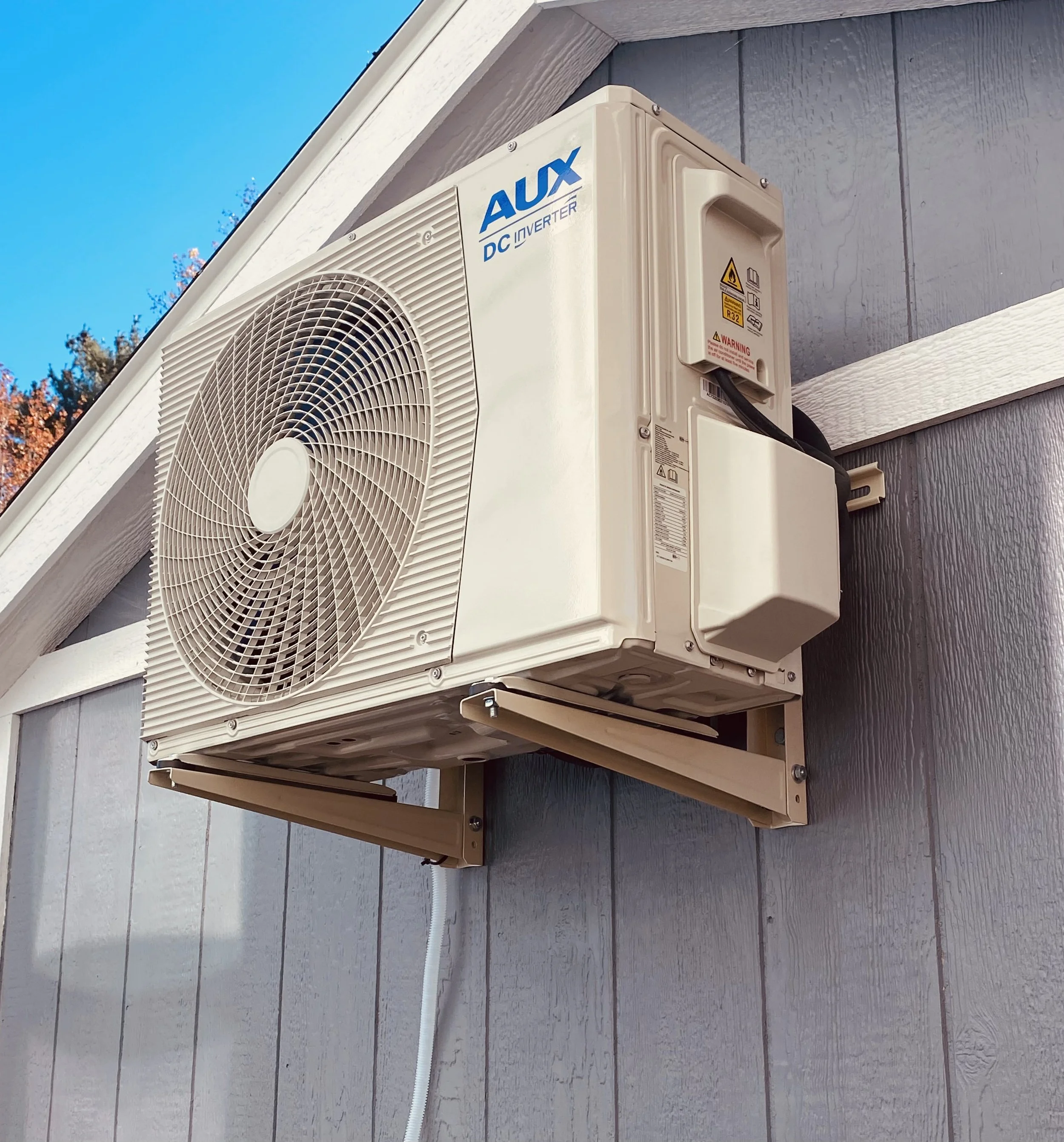 Outdoor air conditioning unit mounted on the exterior wall of a house under a gable roof.
