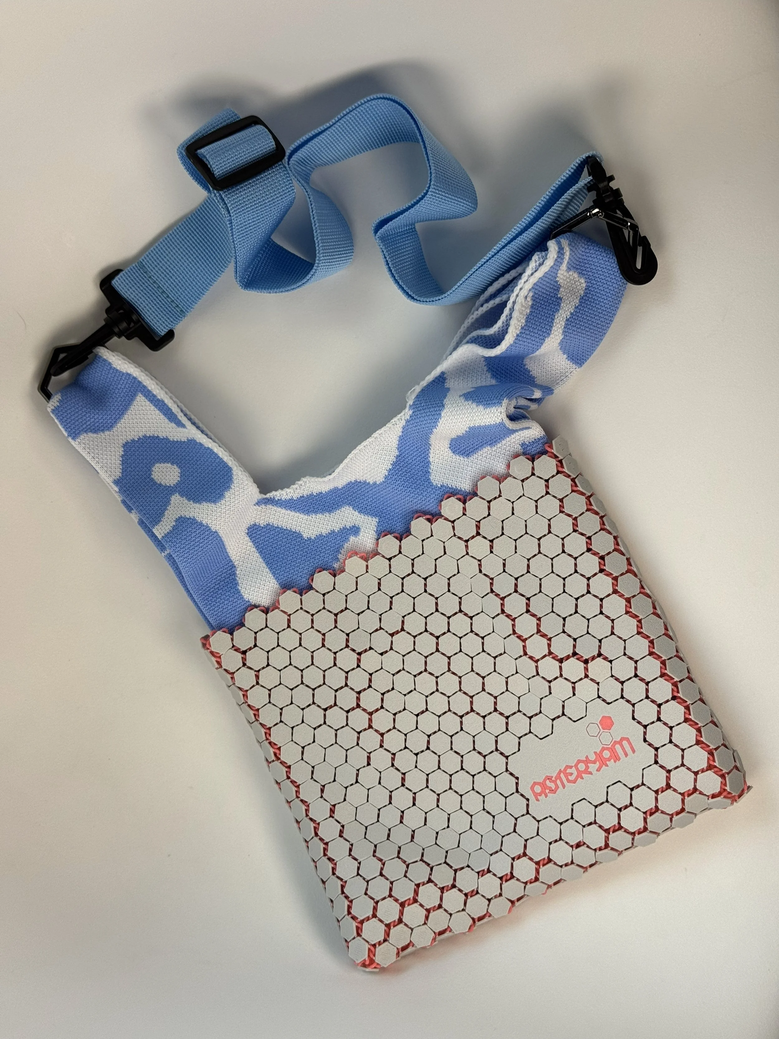 Flat lay of Hexa Sling 3D printed bag with light grey hexagonal shell and blue knitted liner.