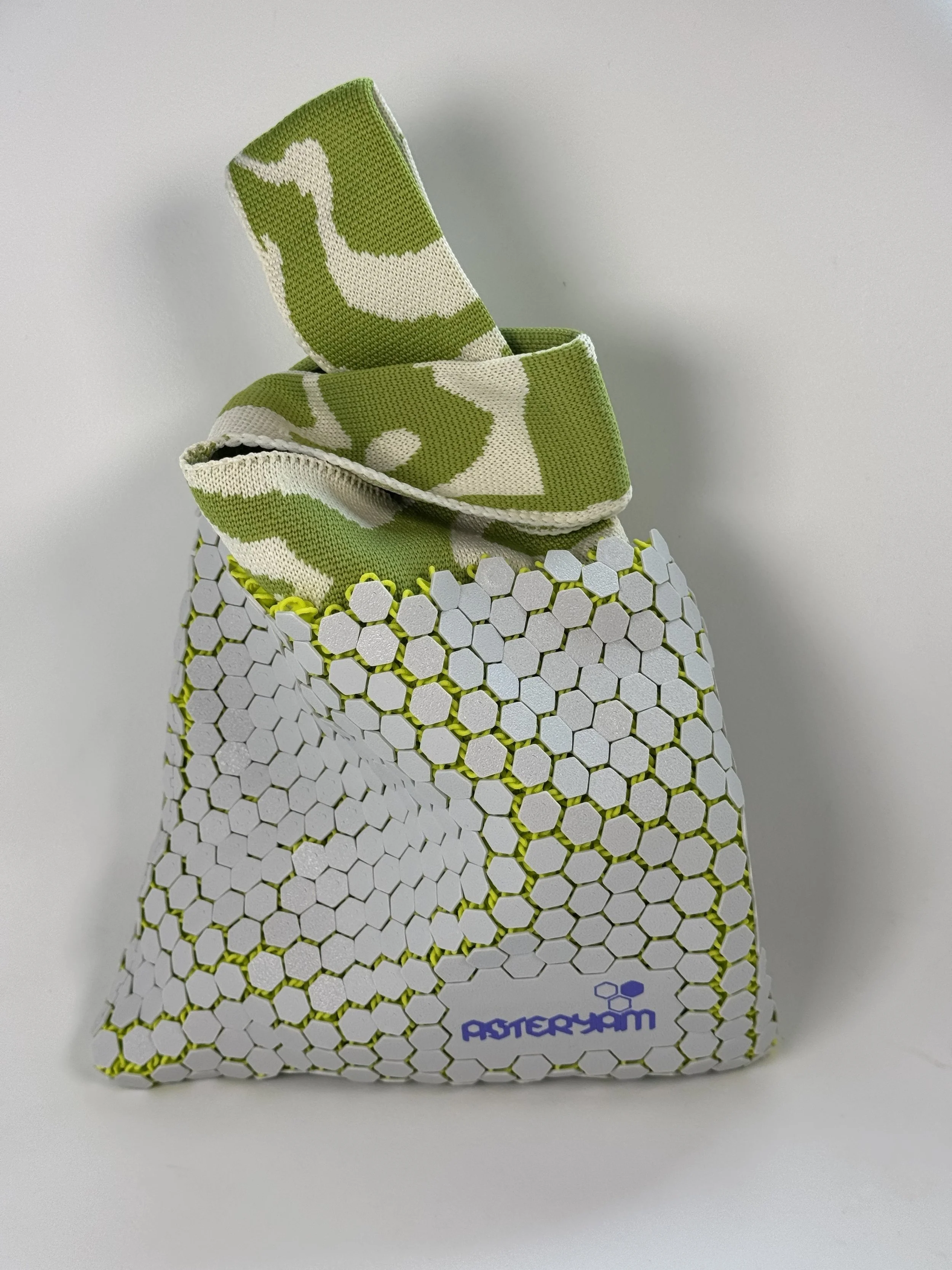 The Hexa Sling styled as a wristlet with knitted handles crossed in a Japanese knot bag style. Demonstrates the flexibility of the 3D printed mesh and the soft drape of the fabric liner.