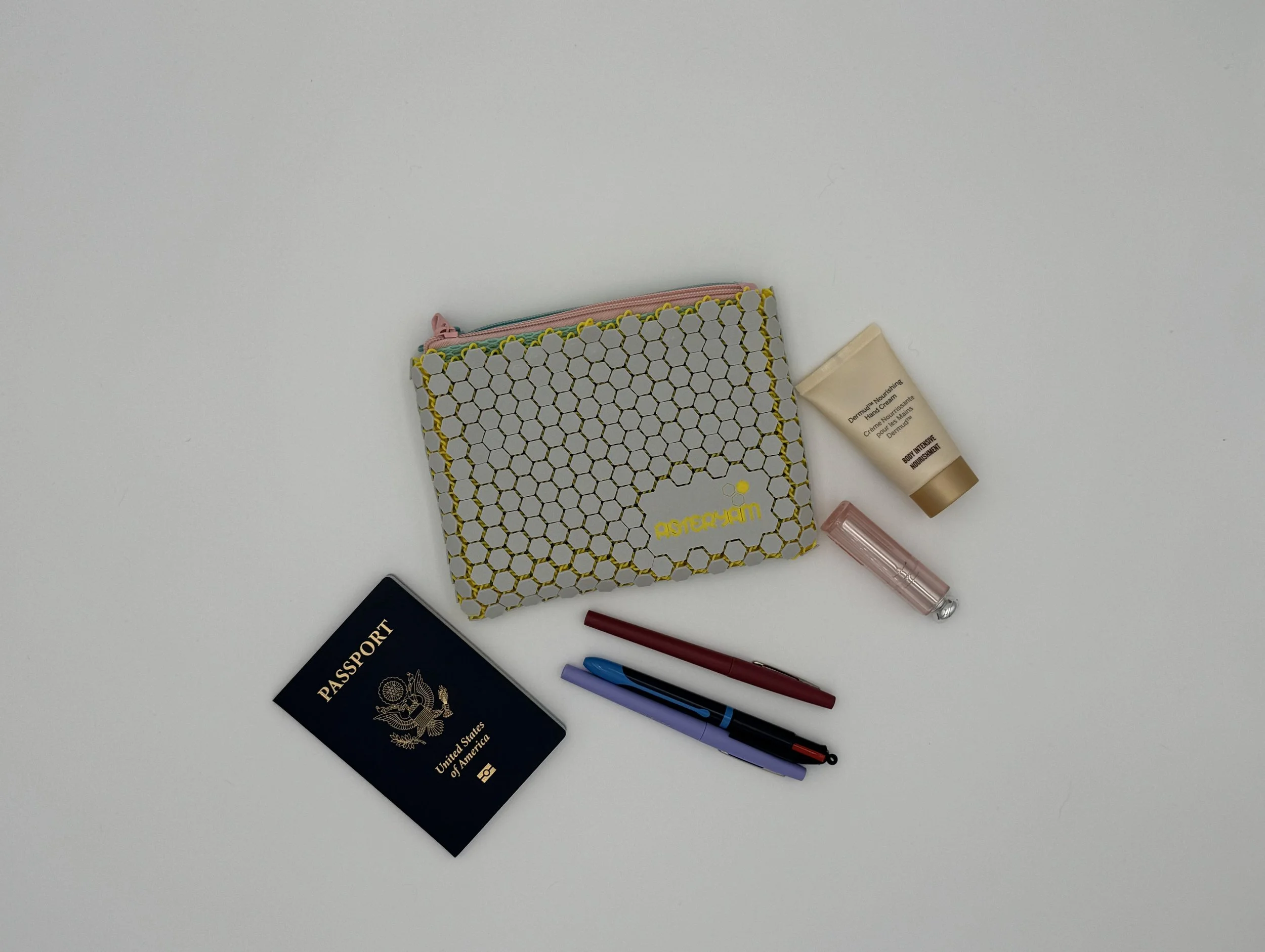 Top-down view of the ASTERYAM HexaDuo surrounded by everyday carry items like a passport and lip gloss, serving as a size reference for the compact travel organizer.