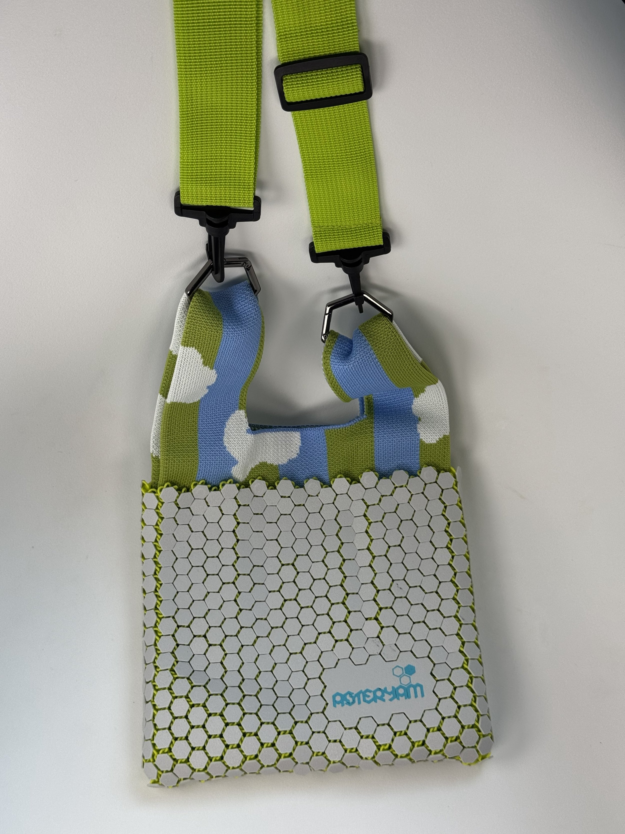 The Hexa Sling bag shown hanging by its detachable green shoulder strap. This view illustrates how the strap clips onto the soft knitted handles, converting the tote into a hands-free crossbody bag.