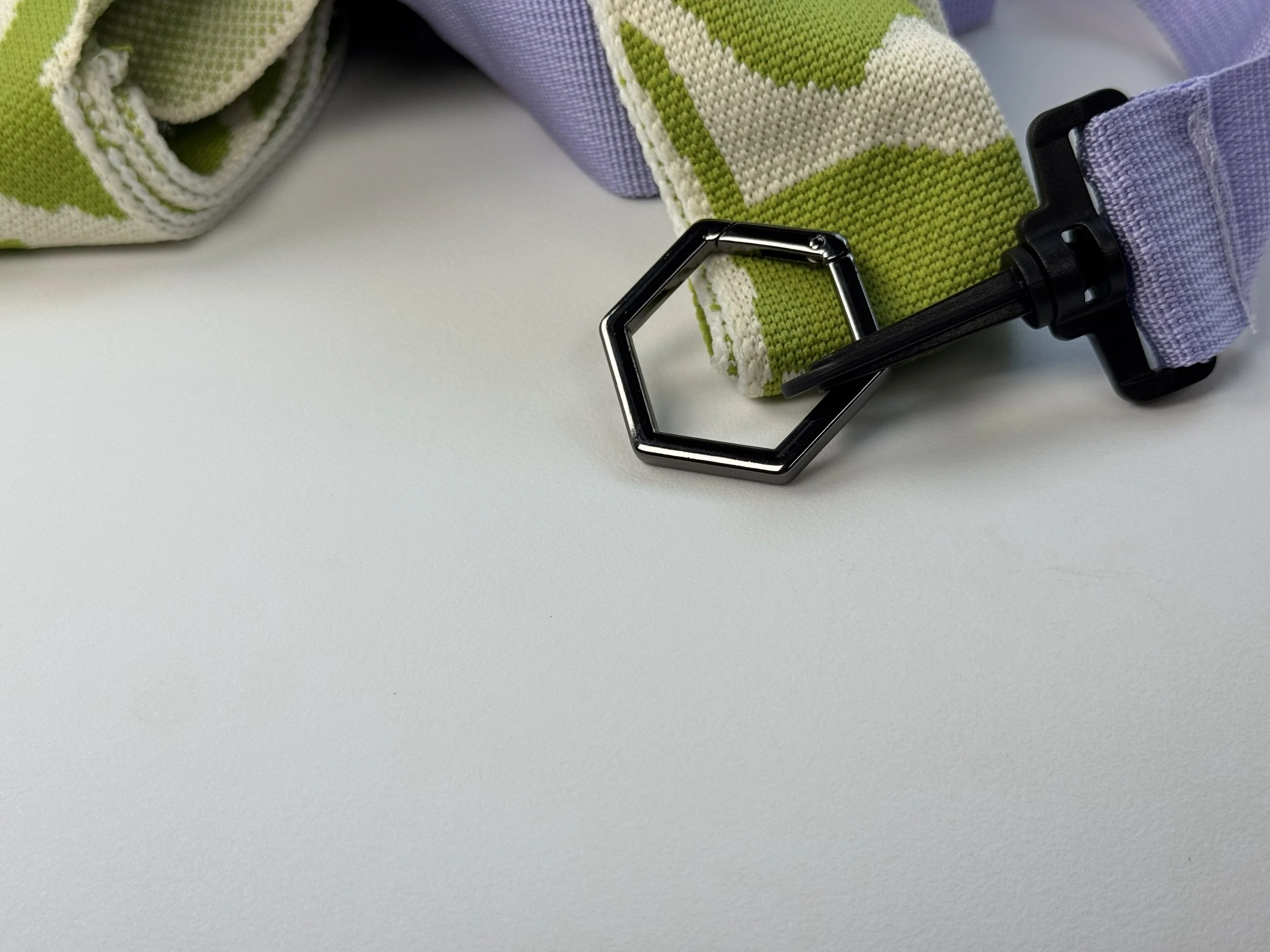 Detail shot of the hexagonal metal hardware connecting the patterned knit strap to the purple adjustable webbing. Highlights the high-quality finish and geometric design theme.
