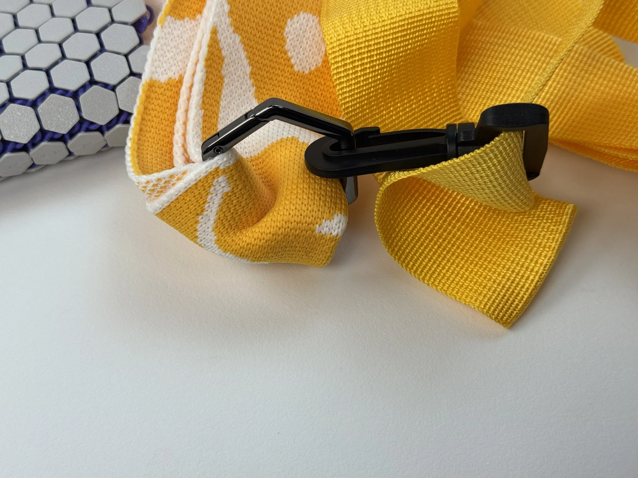 Close-up of black geometric hardware clipped onto soft yellow and white knitted fabric, showcasing material contrast.