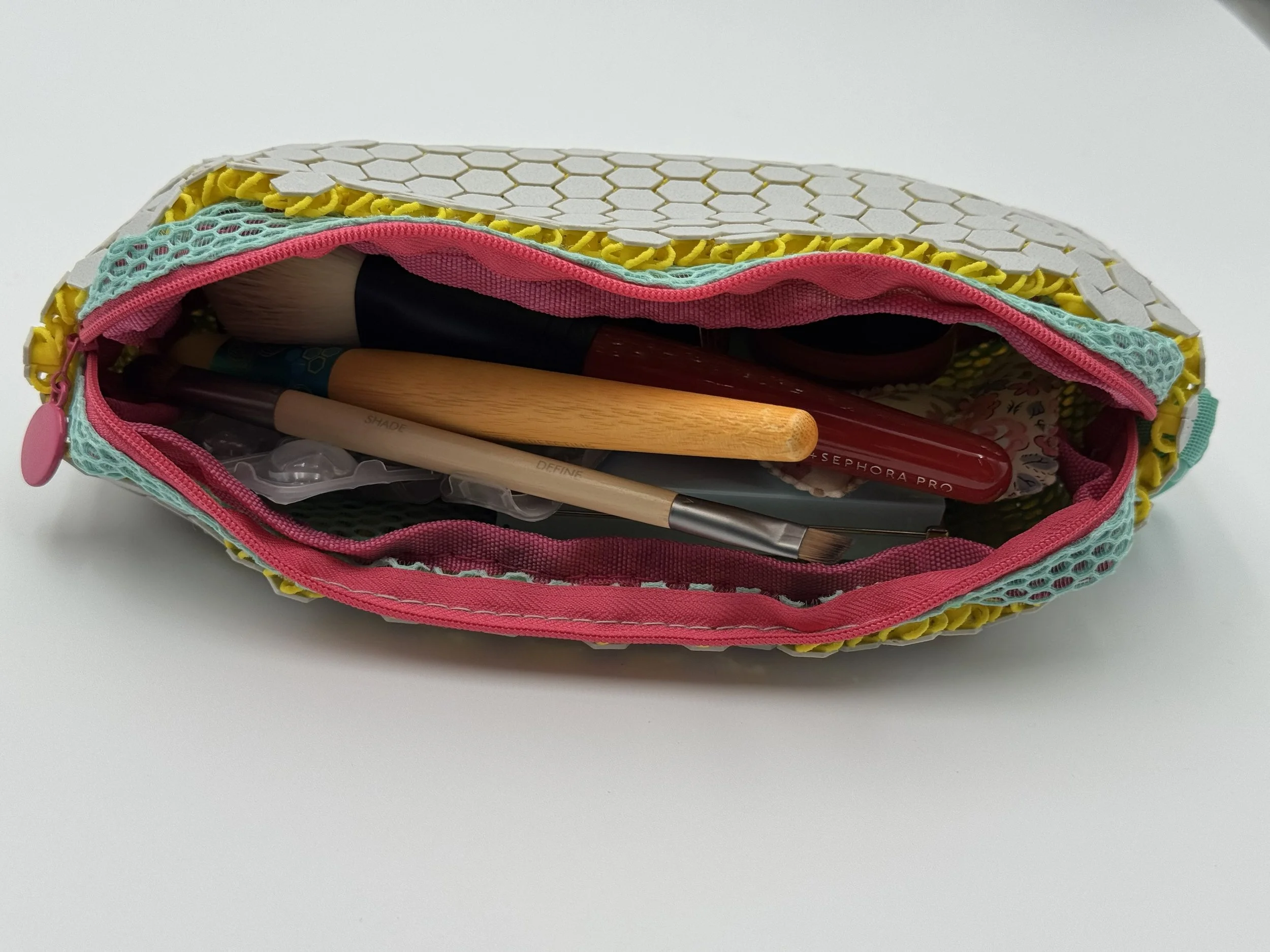 Top view of an open ASTERYAM HexaFlux pouch, revealing the pink zipper tape and mint green nylon mesh lining holding makeup brushes and wooden pencils.