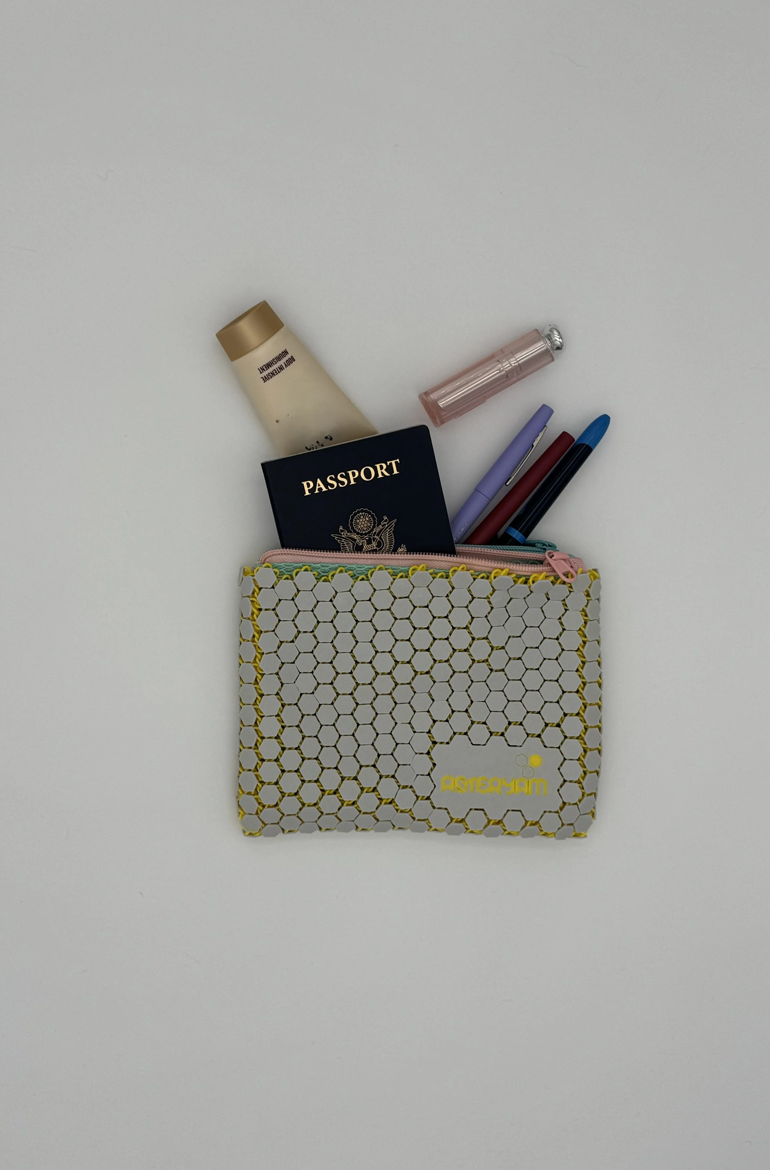 The ASTERYAM HexaDuo bag shown with items tucked inside, demonstrating capacity for a passport, lotion, and pens within the double-zippered nylon lining.