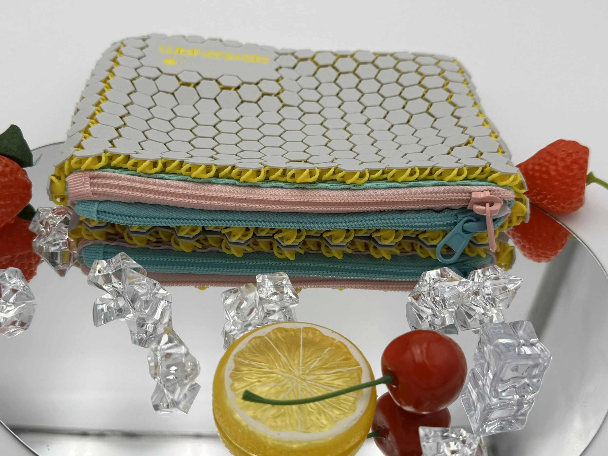 Close-up side view of the HexaDuo bag on a mirrored surface, clearly showing the two separate pastel zipper compartments and the flexible 3D printed structure.