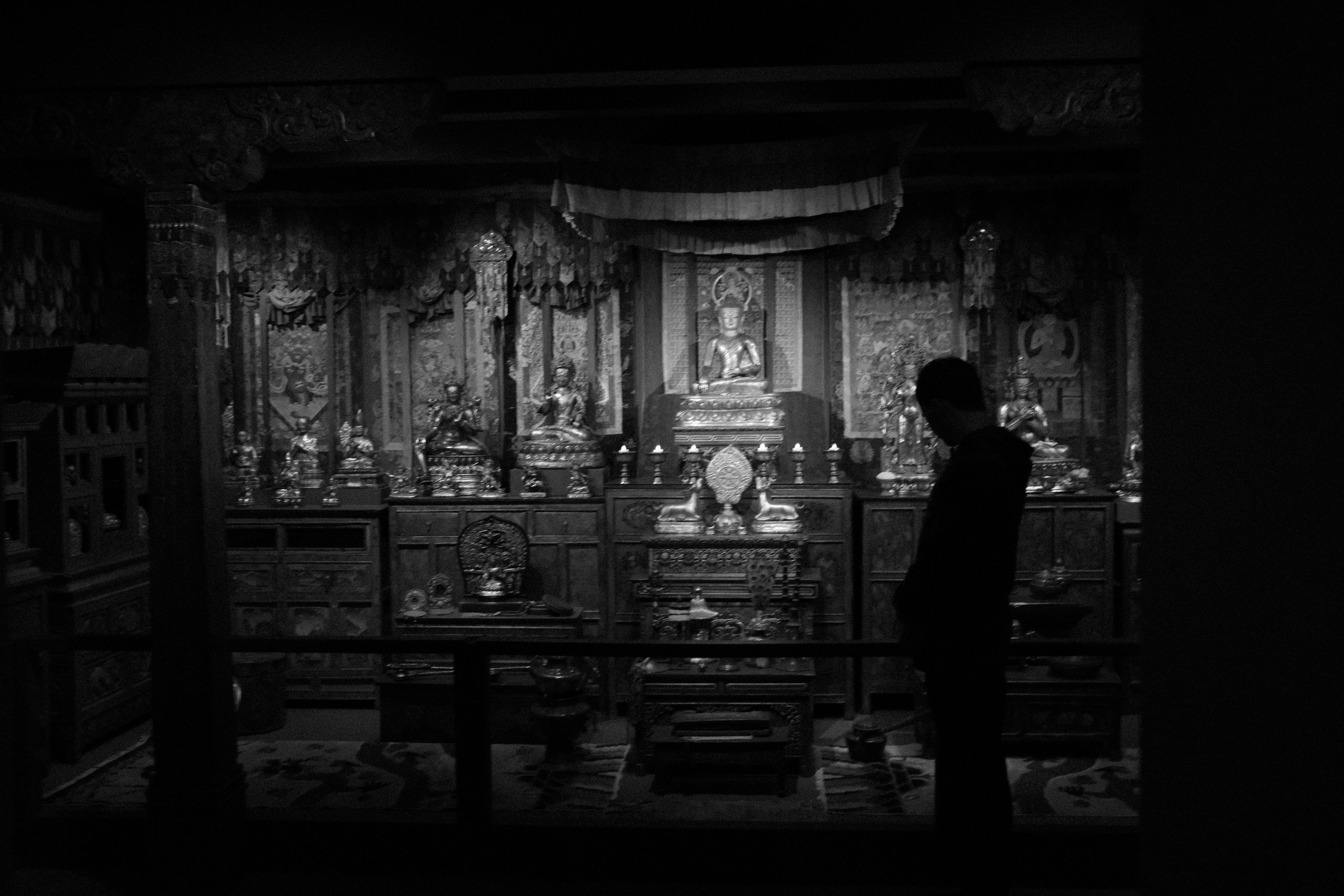 A person standing in front of an ornate altar with multiple statues and religious artifacts in a dimly lit space.