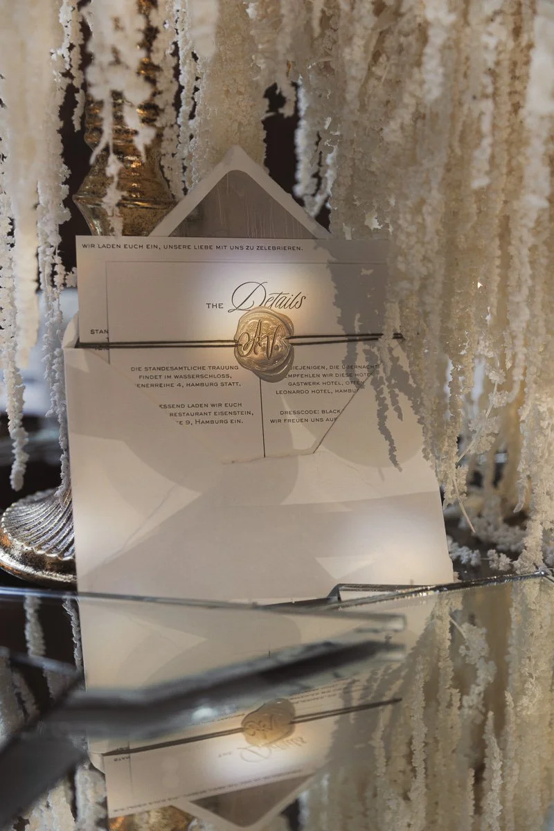 Ein Einladungsschreiben für eine Hochzeit, dekoriert mit Schnee- oder Frost-ähnlicher Dekoration, inklusive einem Brief mit einem goldenen Siegel.