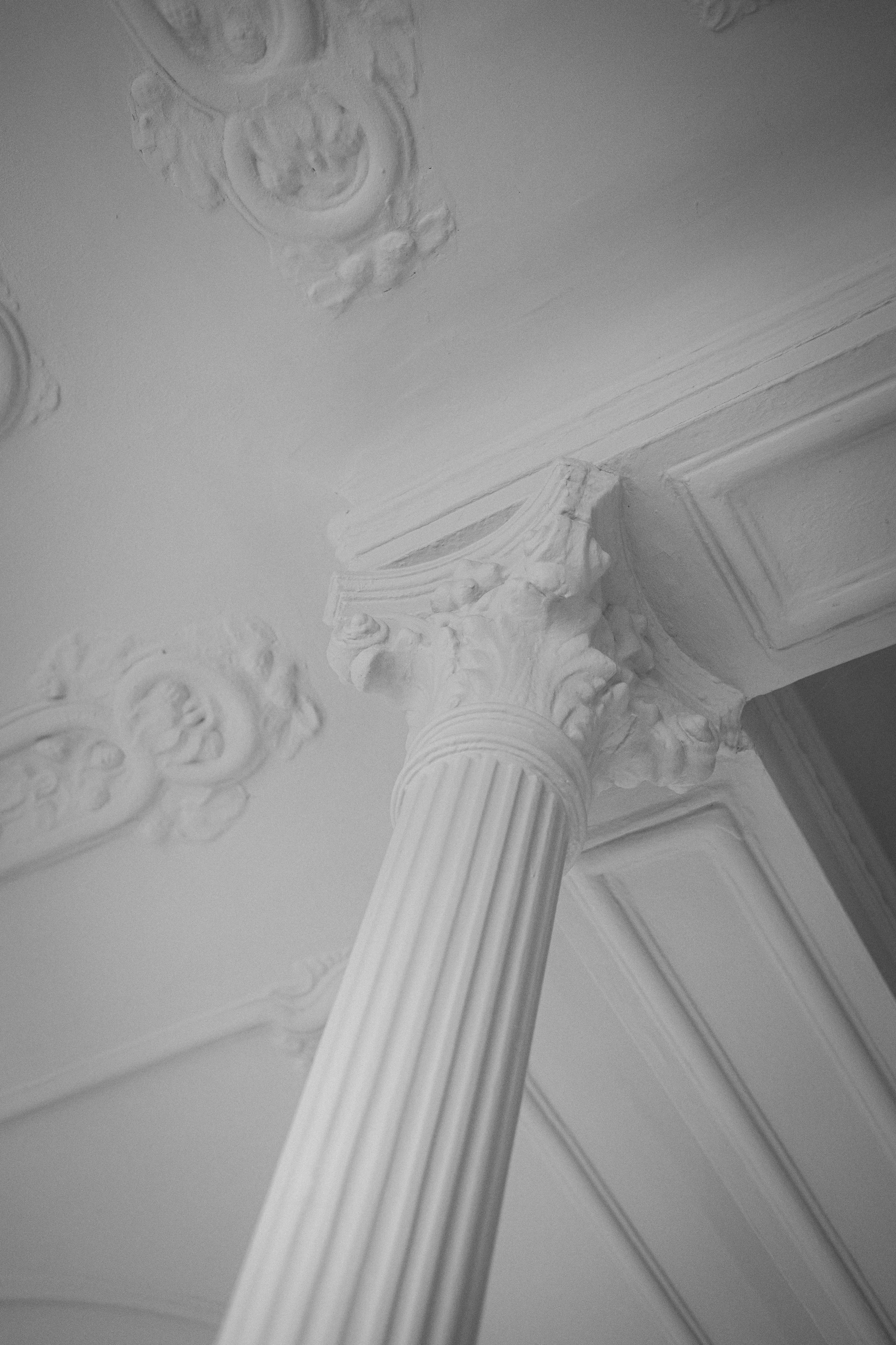 Ein Blick nach oben auf eine Säule im klassizistischen Stil mit Muscheldekoration und einer Deckenverzierung im Hintergrund.