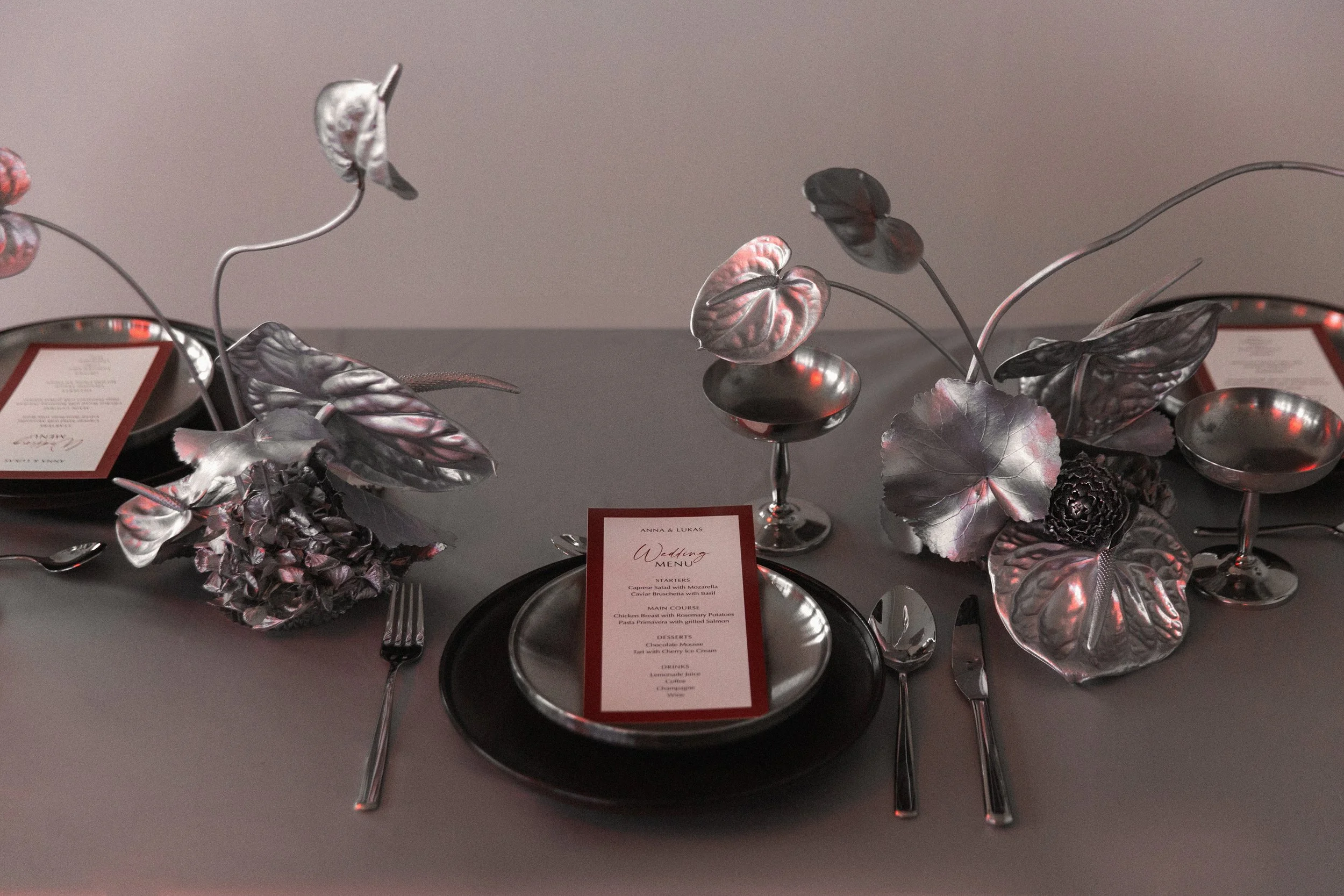 Dekorative, silberfarbene metallische Blumen und Blätter auf einem Tisch, mit Menükarten und Besteck dazu.