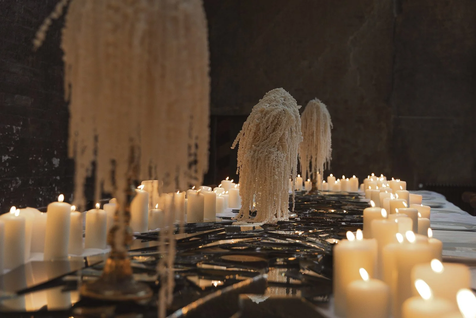 Elegante Tischdekoration mit brennenden Kerzen und weißen, baumähnlichen Skulpturen, die mit Zucker oder Salz bedeckt sind, in einem dunklen Raum.